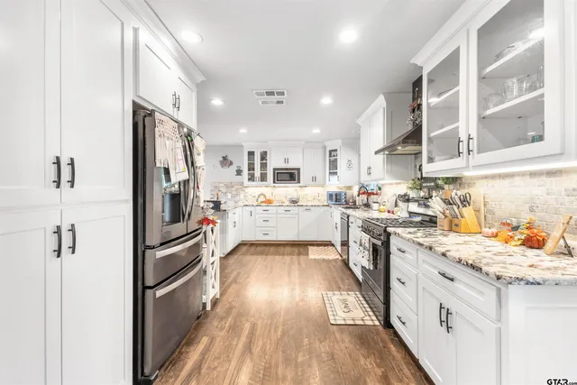 a kitchen with stainless steel appliances kitchen island granite countertop a refrigerator a sink dishwasher a stove and white cabinets with wooden floor