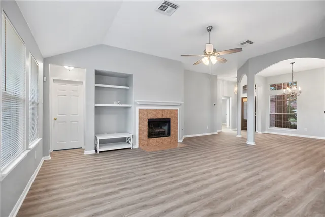 an empty room with wooden floor fireplace and windows