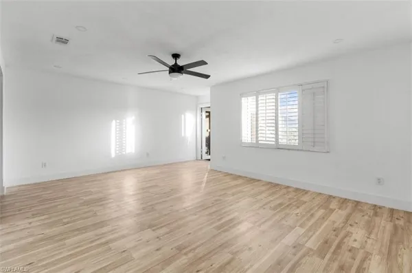 an empty room with wooden floor ceiling fan and windows