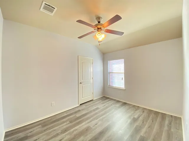 an empty room with wooden floor fan and windows