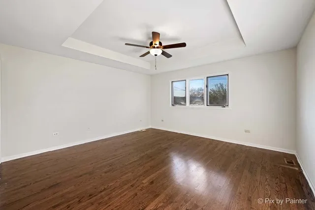 an empty room with wooden floor ceiling fan and windows