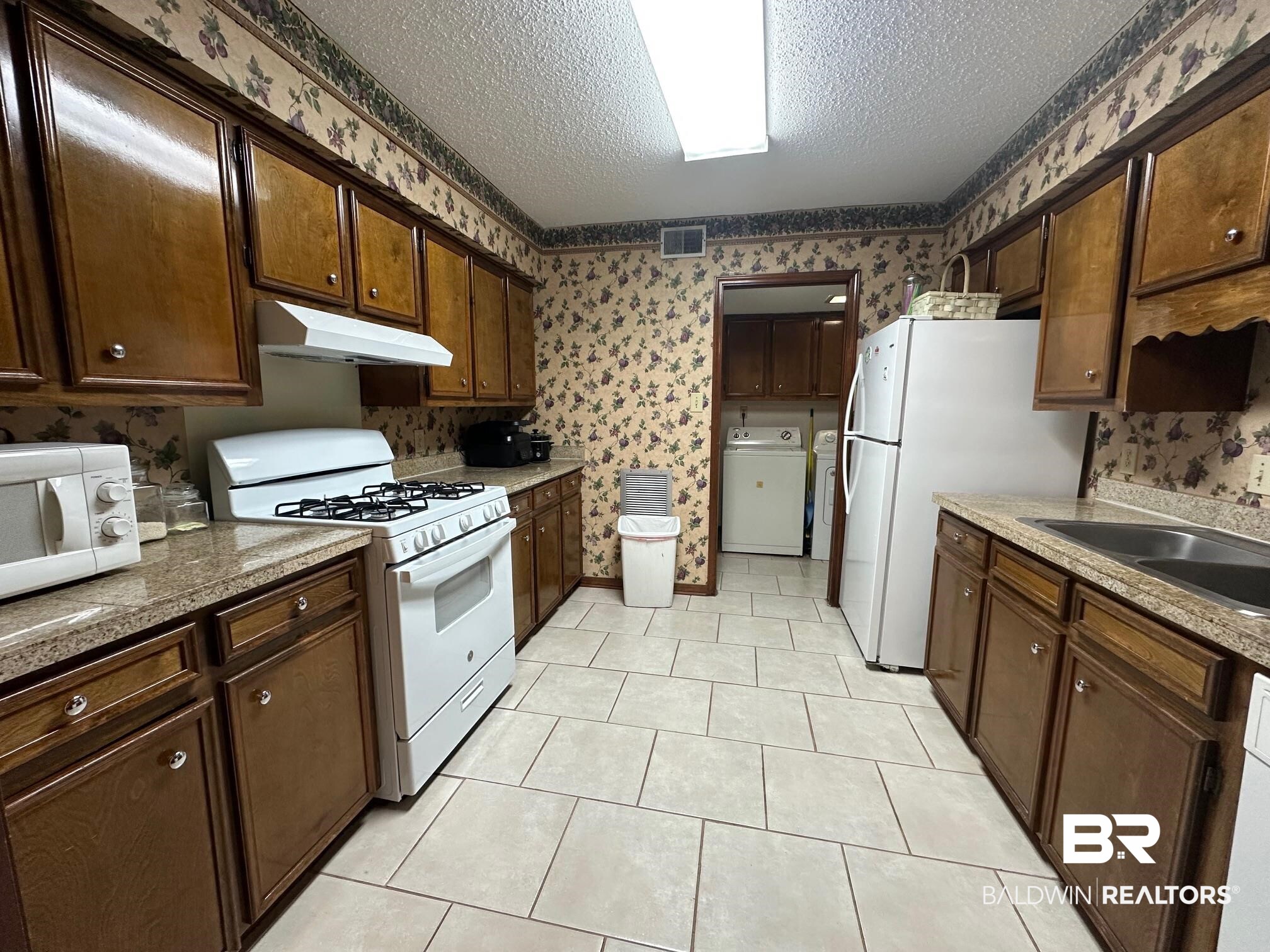 6533 Cedar Bend Court, Unit A Mobile, AL 36608 - Photo 7 of 16 Kitchen with white appliances, a textured ceiling, wallpapered walls, dark wood finish cabinetry, and light countertops