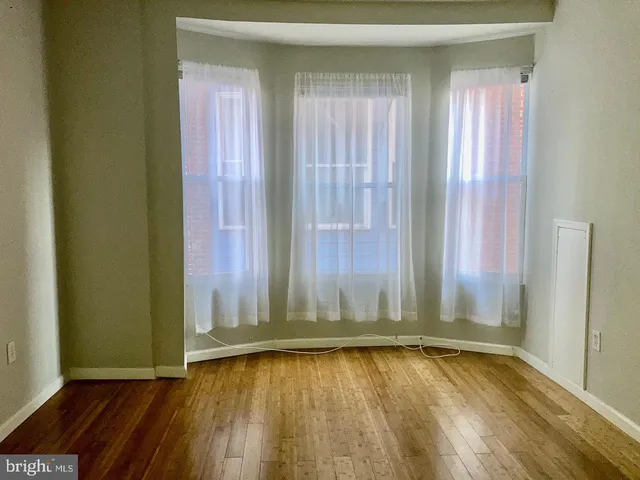 an empty room with wooden floor and windows with curtains
