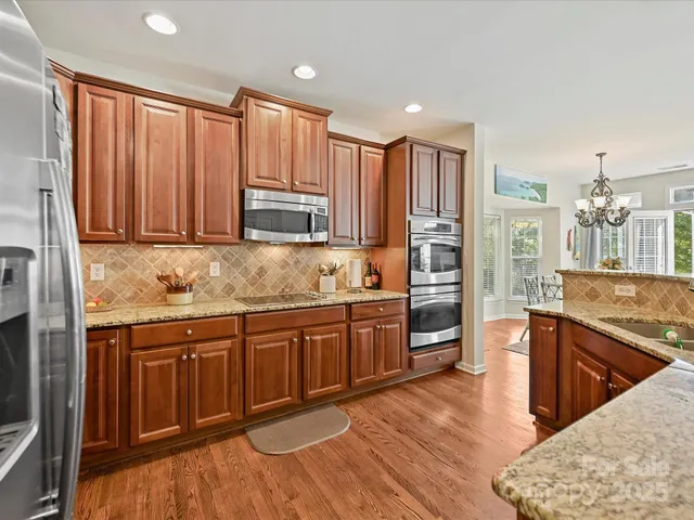 a kitchen with stainless steel appliances granite countertop wooden cabinets a sink and dishwasher a stove with wooden floor