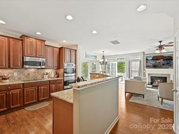 a kitchen with stainless steel appliances granite countertop a stove top oven a sink dishwasher a dining table and chairs with wooden floor