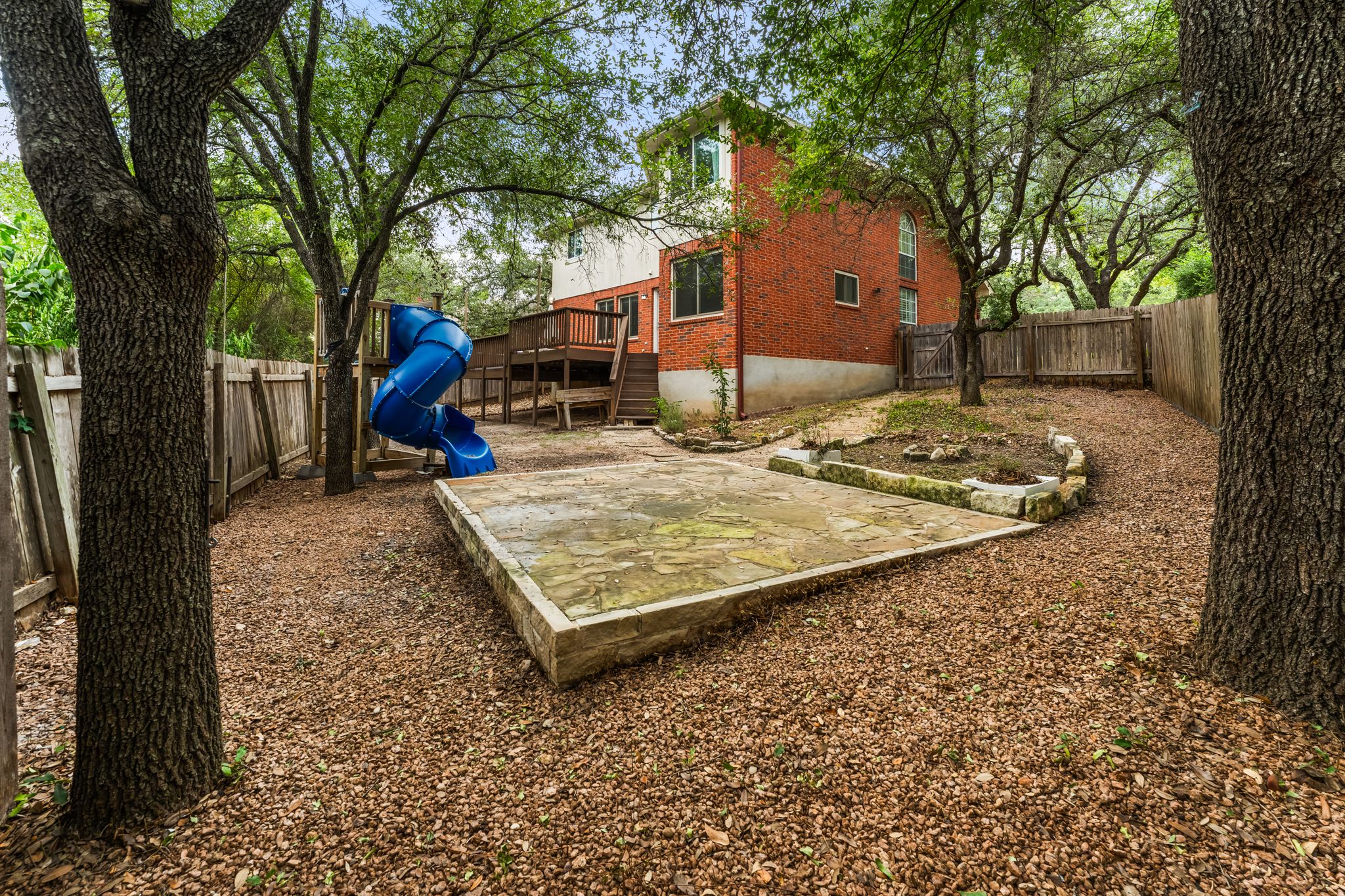 3704 Caney Creek Road Austin, TX 78732 - Photo 34 of 40 A spacious backyard features a stone patio and mature trees, offering a tranquil outdoor retreat.