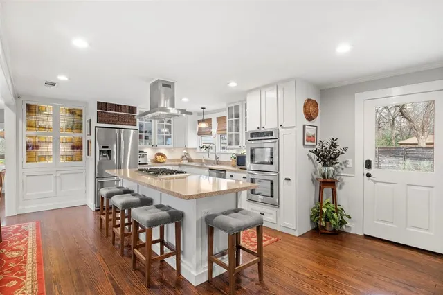 a kitchen with stainless steel appliances granite countertop a refrigerator a stove and white cabinets with wooden floor