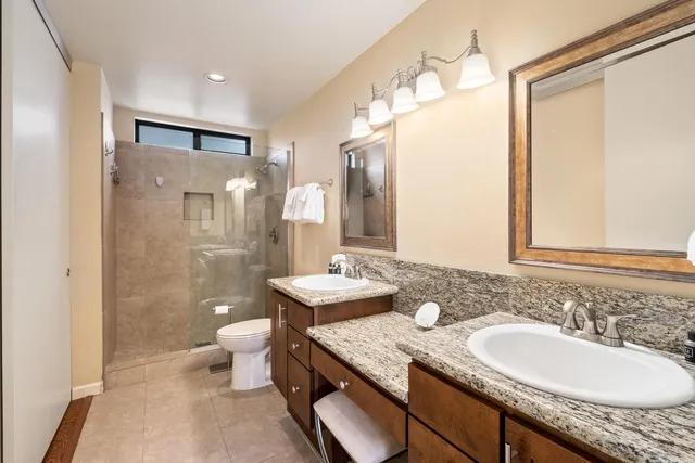 a bathroom with a granite countertop sink a toilet a mirror and shower