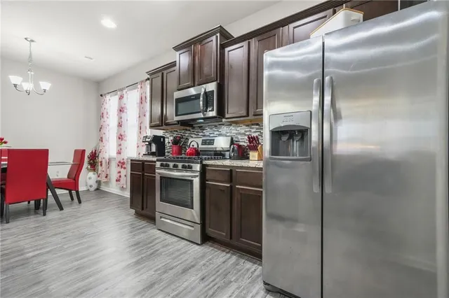 a kitchen with stainless steel appliances granite countertop a refrigerator a stove a sink and a dining table with wooden floor