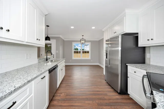 a kitchen with stainless steel appliances granite countertop a refrigerator a stove and a sink with wooden floors