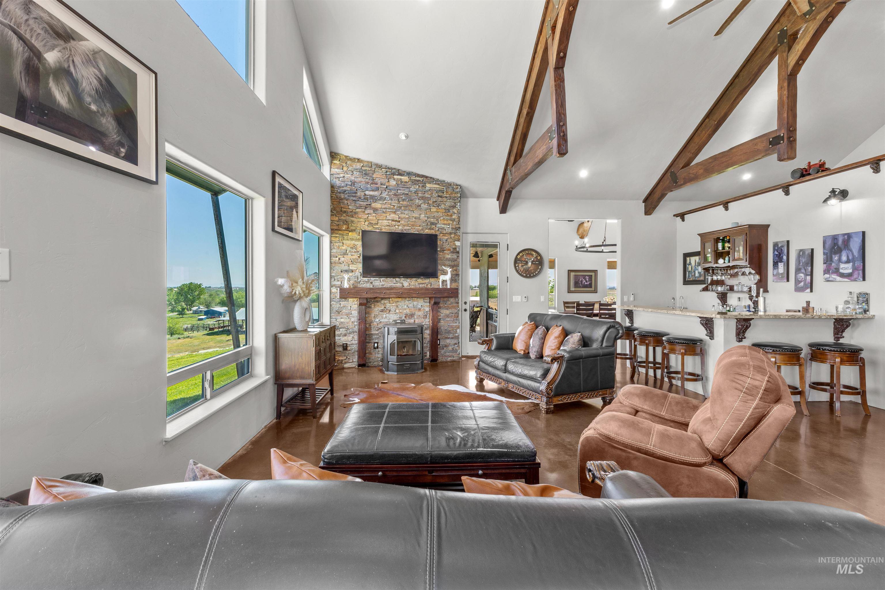 1030 Desert Glen Road Adrian, OR 97901 - Photo 31 of 47 Expansive living area featuring a vaulted ceiling with exposed wood beams, a stone accent wall fireplace with a wood mantle, large windows, and wood-finish flooring