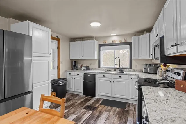 a kitchen with stainless steel appliances granite countertop a stove top oven a sink a refrigerator and white cabinets