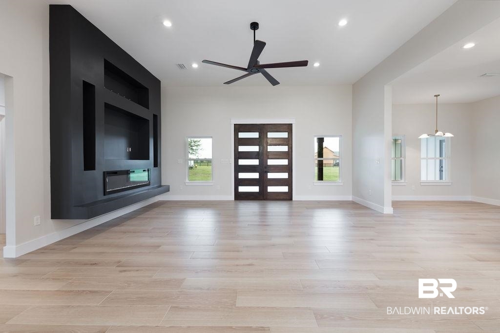 13066 Gopher Court Elberta, AL 36530 - Photo 28 of 38 Spacious open-concept living area featuring light wood-finish flooring, a contemporary built-in media center with an electric fireplace, a dark wood entry door with horizontal glass inserts, high ceilings, and recessed lighting