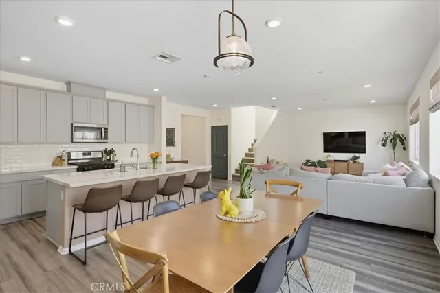 a kitchen with stainless steel appliances granite countertop a stove a refrigerator a kitchen island a dining table and chairs with wooden floor