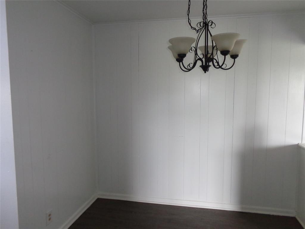 612 South Files Street Itasca, TX 76055 - Photo 13 of 30 Unfurnished dining area with crown molding, dark wood-style floors, a chandelier, and wooden walls