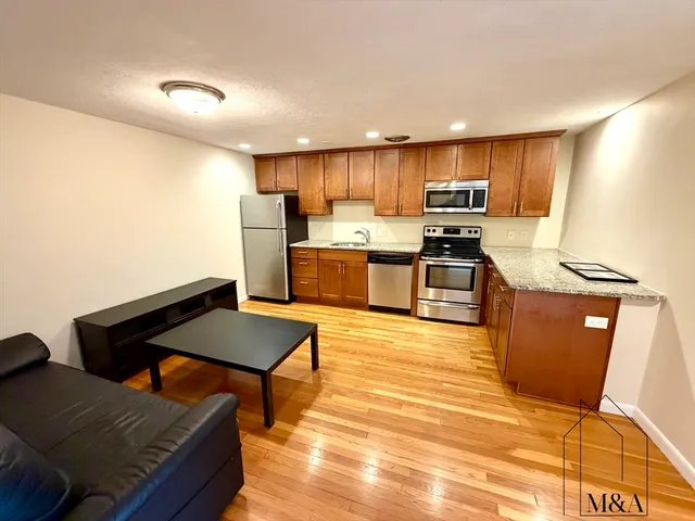 a kitchen with stainless steel appliances kitchen island granite countertop a refrigerator a stove a sink dishwasher and a dining table with wooden floor