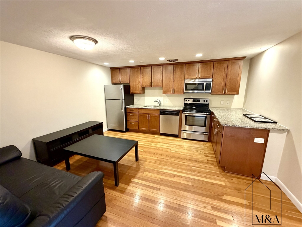 a kitchen with stainless steel appliances kitchen island granite countertop a refrigerator a stove a sink dishwasher and a dining table with wooden floor