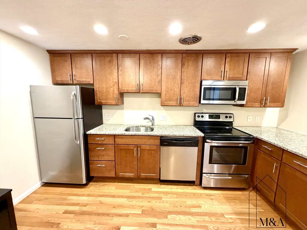 197 Kent Street, Unit 15 Brookline, MA 02446 - Photo 2 of 10 a kitchen with granite countertop a refrigerator and a stove top oven