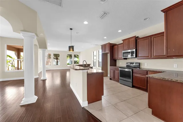 a kitchen with stainless steel appliances granite countertop wooden cabinets a refrigerator a stove a sink and a oven with wooden floor