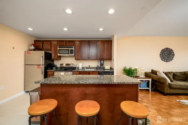 a kitchen with stainless steel appliances granite countertop a sink a stove a kitchen island with chairs and white refrigerator