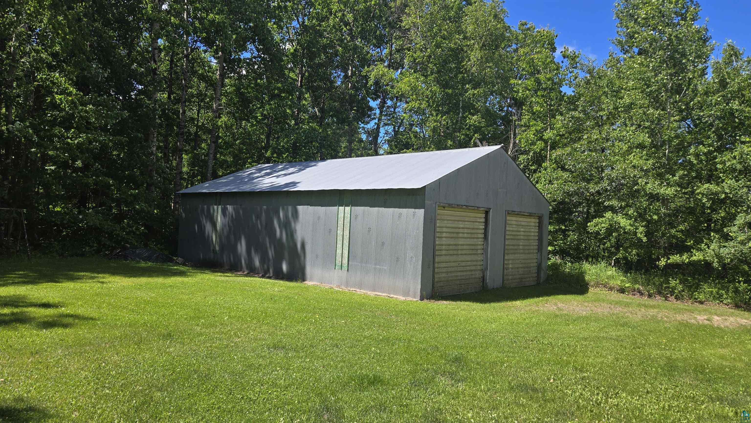 10614 Moose Lake Road Orr, MN 55771 - Photo 6 of 44 Detached two-car garage with a metal roof and two roll-up doors, set on a grassy lot surrounded by mature trees