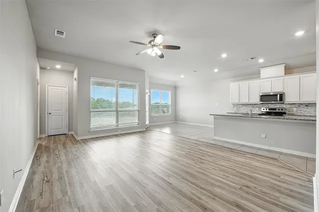 a view of an empty room with wooden floor and a kitchen