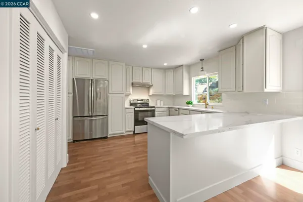 a kitchen with stainless steel appliances granite countertop a refrigerator a sink a stove a microwave and white cabinets with wooden floor