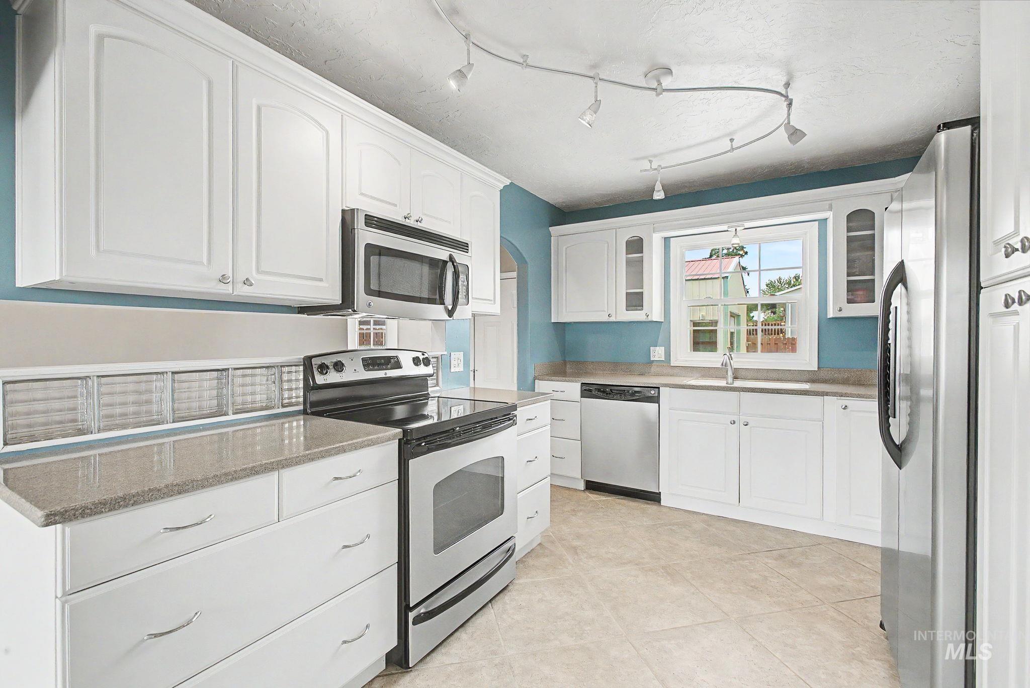 3314 6th Street Lewiston, ID 83501 - Photo 12 of 50 Kitchen featuring white cabinetry, stone-finish countertops, stainless steel appliances, tile flooring, and track lighting