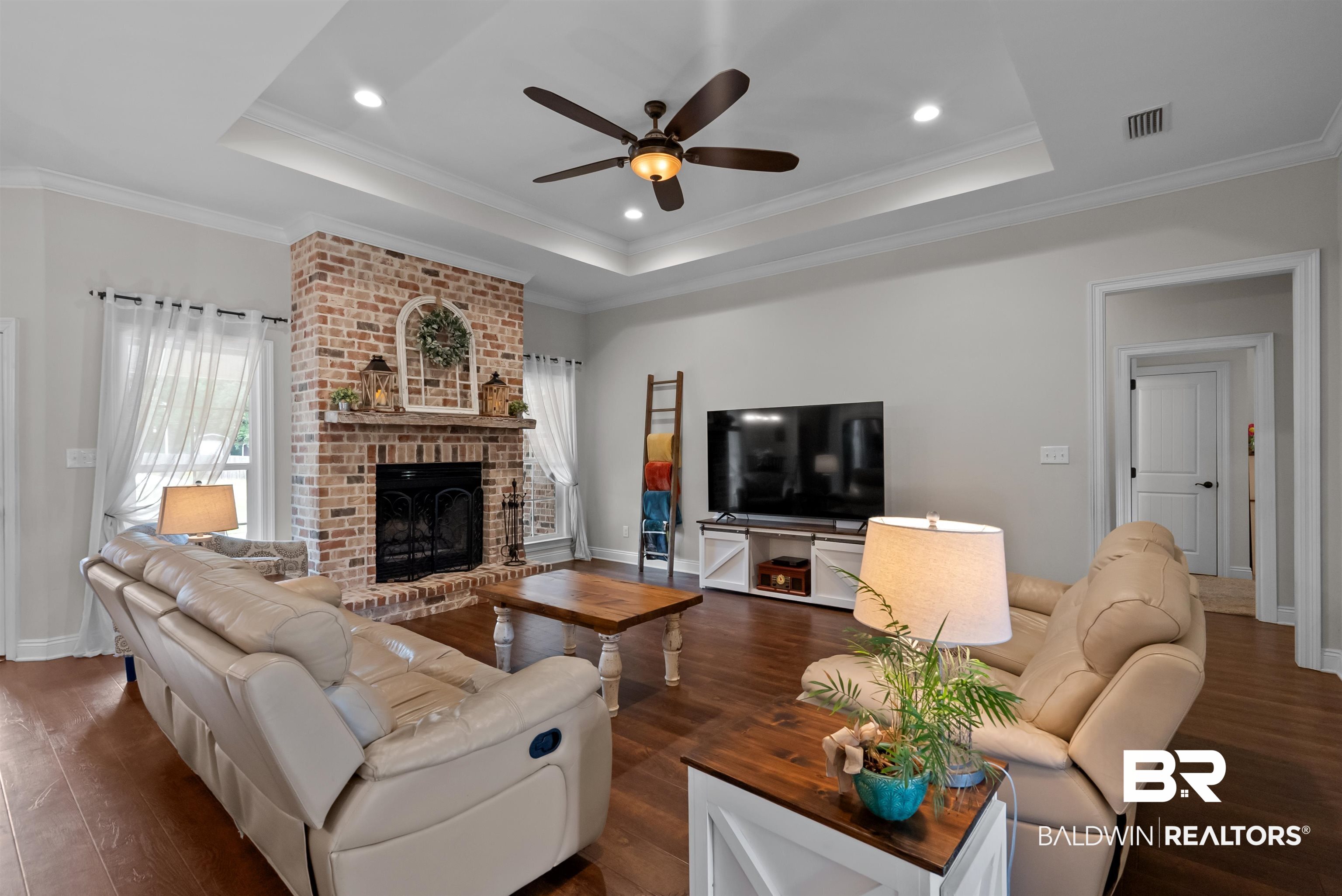 12070 Comalander Road Fairhope, AL 36532 - Photo 8 of 50 Living area featuring a brick fireplace, wood-finish flooring, a tray ceiling with recessed lighting, crown molding, and a ceiling fan