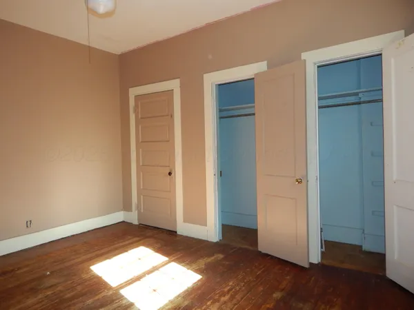 an empty room with wooden floor closet and windows