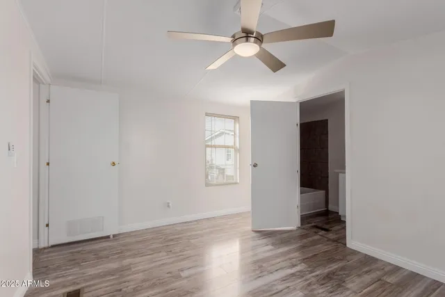 an empty room with wooden floor chandelier fan and windows