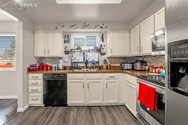 a kitchen with stainless steel appliances granite countertop a refrigerator a stove top oven a sink dishwasher and white cabinets with wooden floor