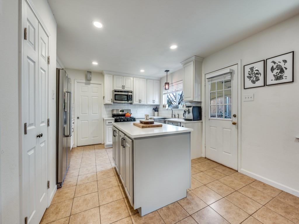 9835 Estate Lane Dallas, TX 75238 - Photo 13 of 25 Kitchen featuring hanging light fixtures, white cabinetry, decorative backsplash, stainless steel appliances, and a kitchen island