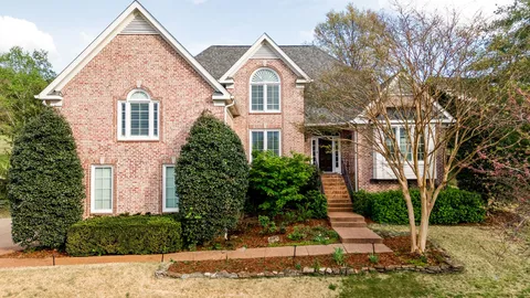 a view of a brick house next to a yard with large trees