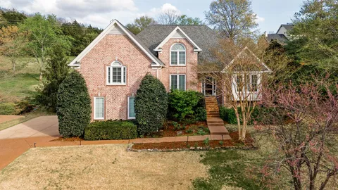 a view of a white house next to a yard with big trees