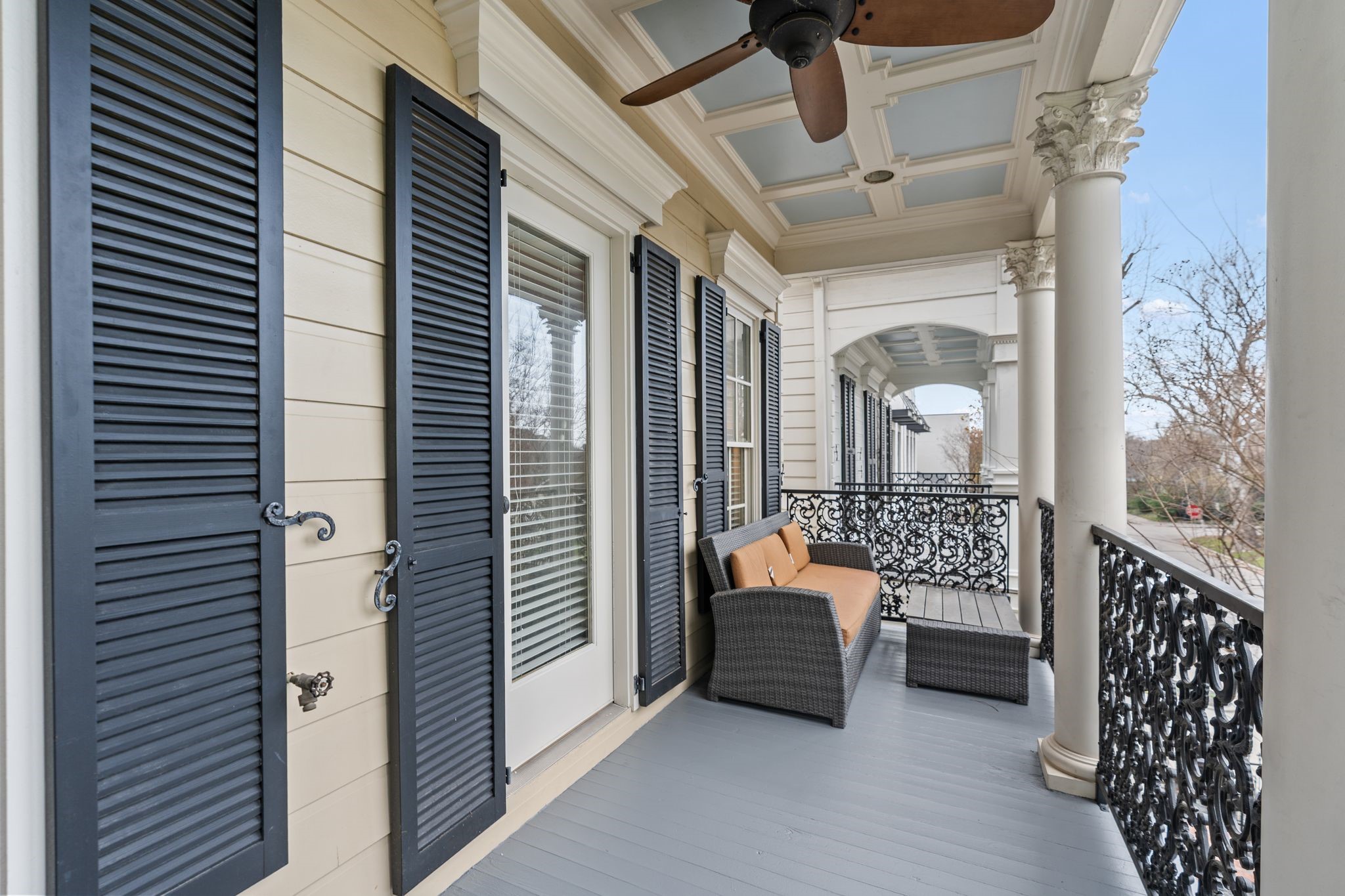 316 Aurora Street Houston, TX 77008 - Photo 20 of 31 Accessible from the secondary bedroom, this expansive covered balcony is defined by its coffered ceiling with beadboard detailing, a ceiling fan, decorative iron railings, and stately columns, while black shutters and French doors enhance the classic exterior and curb appeal. Generous in scale and overlooking the street below, it provides a true extension of the living space outdoors.