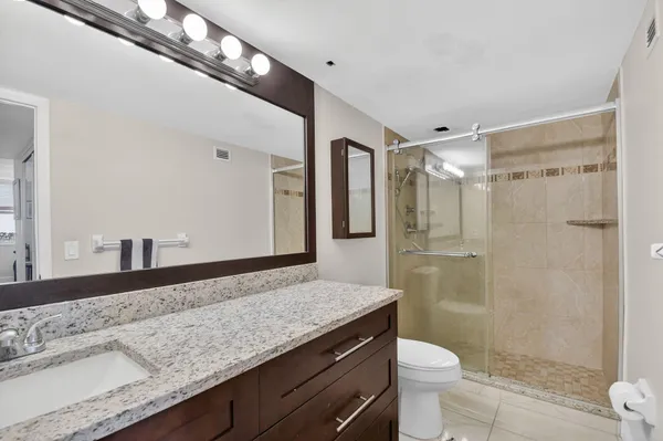 a bathroom with a granite countertop sink a toilet a mirror and shower