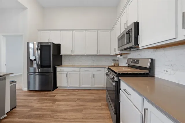 a kitchen with stainless steel appliances granite countertop a refrigerator stove and white cabinets with wooden floor