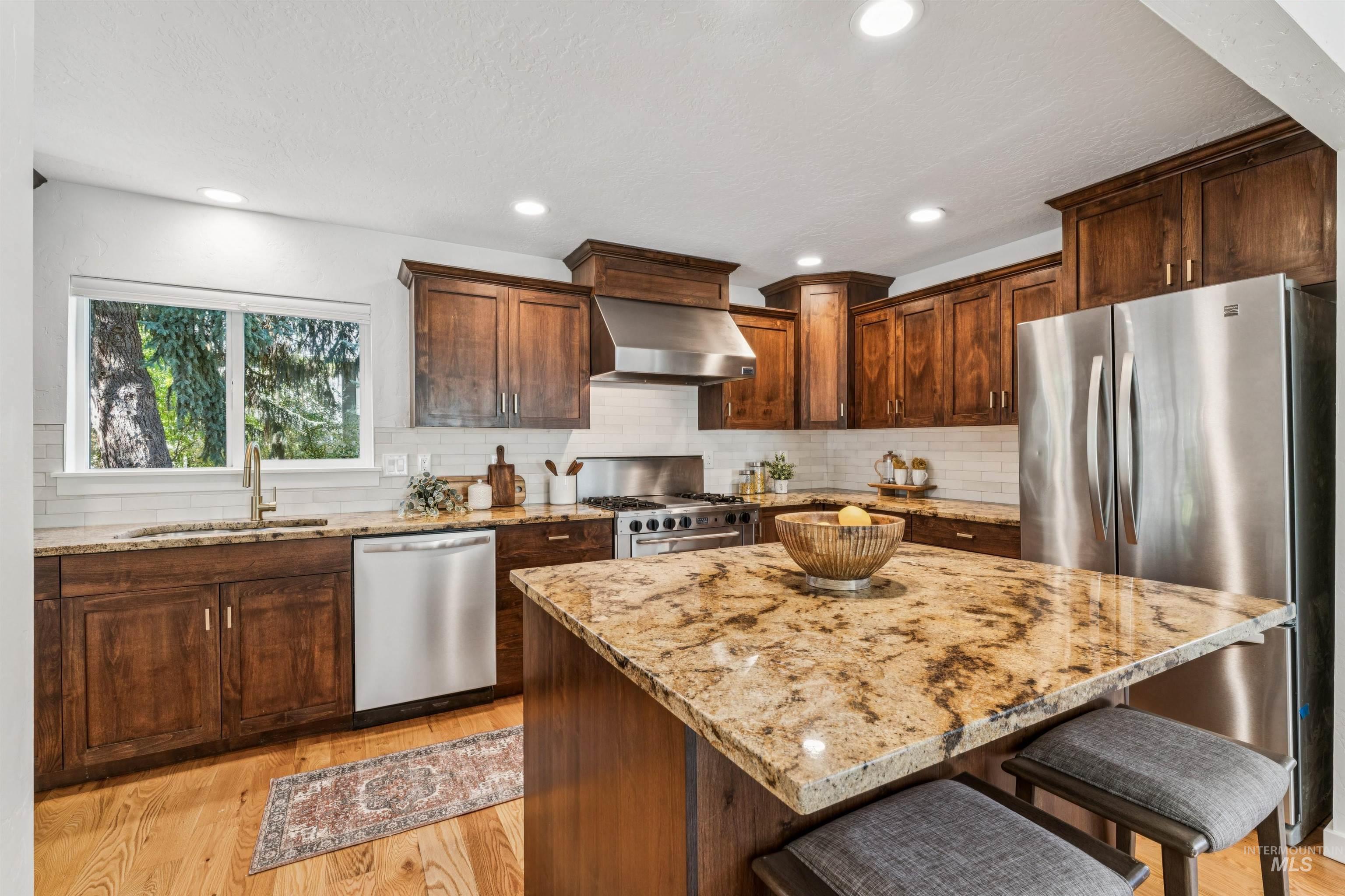 2419 West Hill Road Boise, ID 83702 - Photo 5 of 50 Kitchen featuring a breakfast bar, light wood-type flooring, appliances with stainless steel finishes, wall chimney range hood, and decorative backsplash