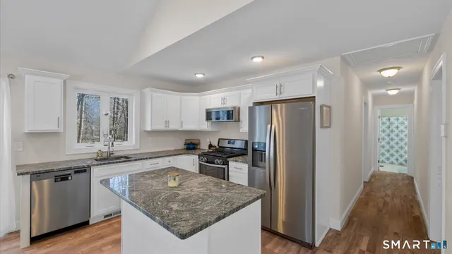 a kitchen with stainless steel appliances granite countertop a stove top oven a sink dishwasher a dining table and chairs with wooden floor