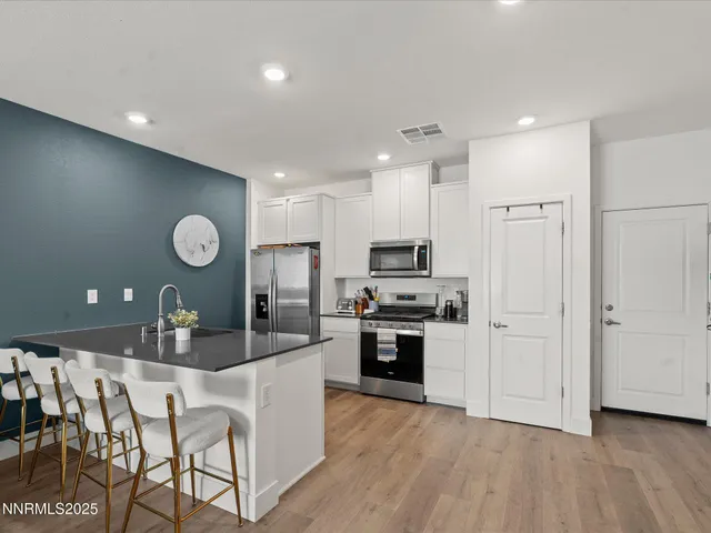 a kitchen with stainless steel appliances granite countertop a stove a sink a refrigerator and white cabinets with wooden floor