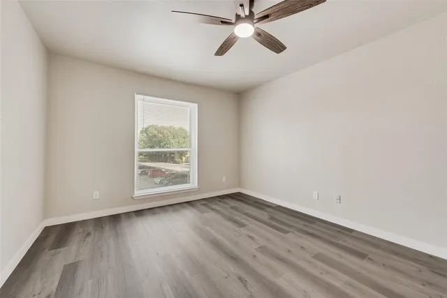 an empty room with wooden floor fan and windows