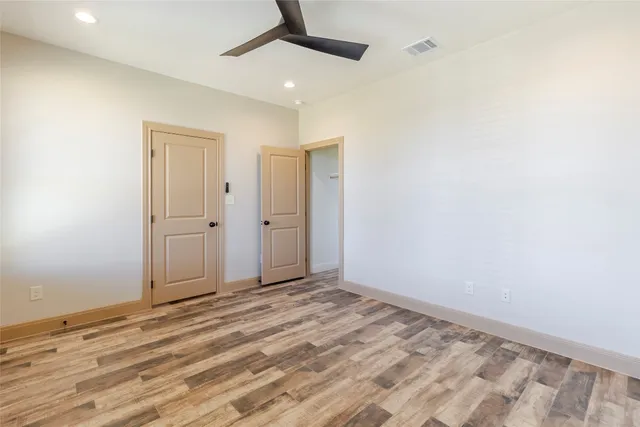 an empty room with wooden floor ceiling fan and windows