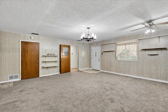 an empty room with chandelier fan and windows