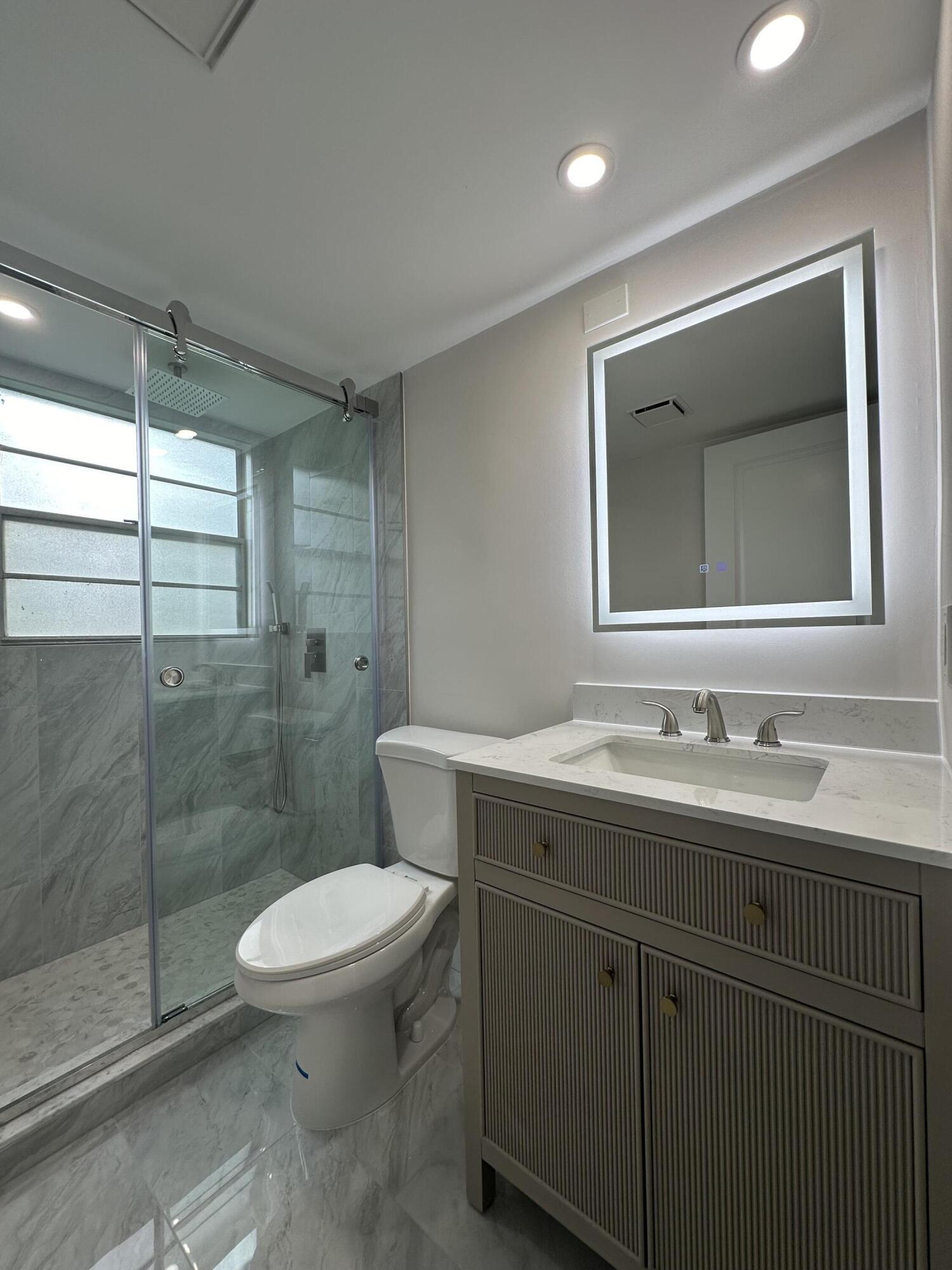 256 Suffolk F Boca Raton, FL 33434 - Photo 4 of 24 a bathroom with a toilet sink vanity and mirror