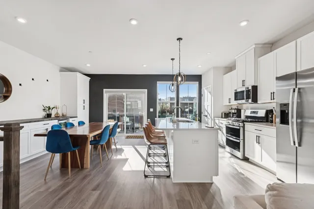 a kitchen with stainless steel appliances kitchen island granite countertop a stove a refrigerator a kitchen island a island and couches with wooden floor