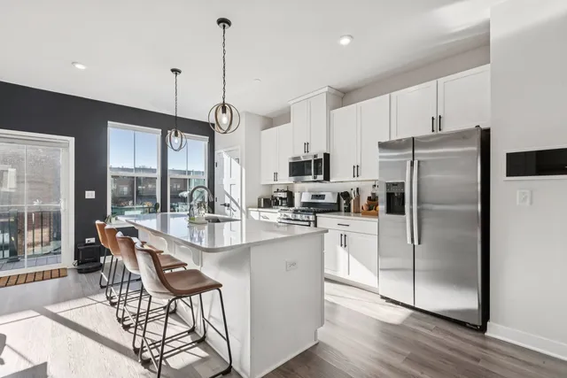 a kitchen with stainless steel appliances granite countertop a refrigerator a sink a stove a dining table and chairs