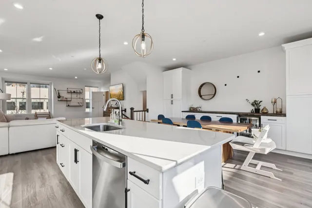 a large white kitchen with a stove a sink a kitchen island with chairs and wooden floor