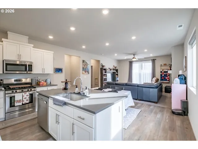 a kitchen with stainless steel appliances kitchen island granite countertop a stove a sink a refrigerator and white cabinets with wooden floor