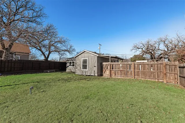 a white house with a big yard and large trees with wooden fence